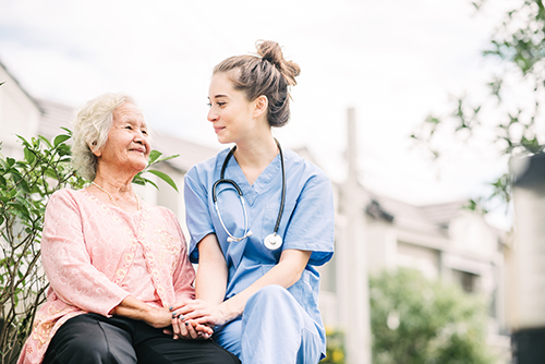 Nurse in blue scrubs sitting outside with Asian elderly woman